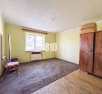 Jednoduchý pokoj v rodinném domě s kobercem a dřevěným nábytkem.