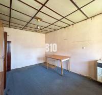 Interiér pokoje v rodinném domě, obsahující koberec, skříně a stůl.