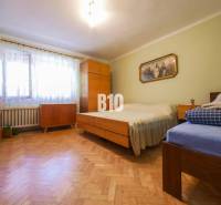 Ložnice s dřevěnou podlahou a jednoduchým nábytkem v rodinném domě.