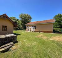 Dvůr rodinného domu v Nových Sadech se dvěma budovami a studnou, obklopený zelení.