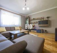 Obývací pokoj s rohovou sedačkou, dřevěné parkety, dekorativní police a osvětlení v rodinném domě.