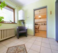 Interiér rodinného domu s předsíní, rostlinou, křeslem a výhledem do kuchyně.