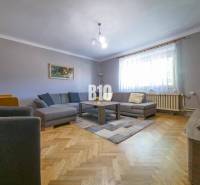 Obývací pokoj v rodinném domě s hnědou podlahou, šedou sedačkou a velkým oknem.