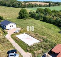 Záběr na pozemek pro bydlení v Čeľadicích zahrnuje dům, zeleň a auta.