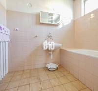 Koupelna v rodinném domě s vanou a světlými obklady na stěnách.