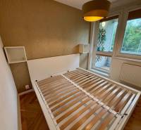 Ložnice s postelí a velkým oknem, 2pokojový byt s podlahou s dřevěným dekorem.