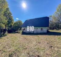 Chata v Lackově obklopená přírodou, s modrou střechou, slunečný den.