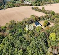 Chata v Lackově obklopená lesem a poli, klidná venkovská krajina.