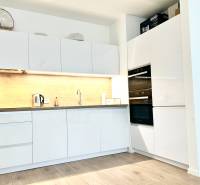 Kuchyně v 2-pokojovém bytě s bílými skříňkami a podlahou s dřevěným dekorem.