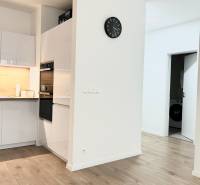 Kuchyně v 2-pokojovém bytě s dřevěným dekorem podlahy a bílým nábytkem.