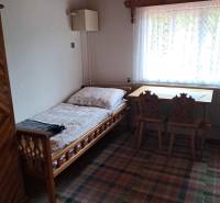 Pokoj v rodinném domě s postelí, oknem, stolem a židlemi.