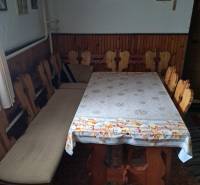 Jídelna v rodinném domě s dřevěnými židlemi a stolem, stěnu zdobí obrazy a kříž.