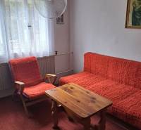 Pokoj v rodinném domě s červenými křesly, stolem a záclonovými závěsy.