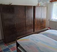 Ložnice v rodinném domě s postelí, skříněmi a kobercem s barevným vzorem.