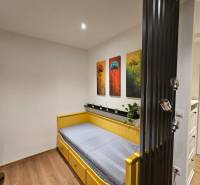 Garsonka s jednolůžkovou postelí, malbami stromů a podlahou s dřevěným dekorem.