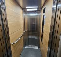 Interiér výtahu s panely s dřevěným dekorem a nerezovými prvky.