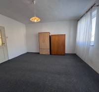 Pokoj s kobercovou podlahou, bílými stěnami, dvěma skříněmi a velkým oknem.