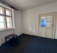 Pokoj s tmavým stolem, oknem a bílými dveřmi v rodinném domě.