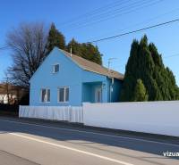 Modrý rodinný dům v Kunově, Senica, u hlavní cesty, obklopený zelenými stromy.