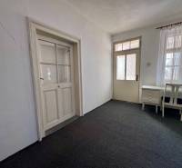 Interiér rodinného domu s kobercem, psacím stolem a křeslem, bílé stěny.