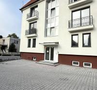 Budova na Sadové ulici v Senici s bílou fasádou a dlážděným parkovištěm.