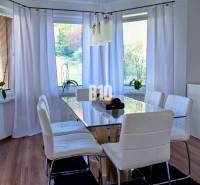 Jídelní kout s prosvětleným interiérem, skleněným stolem a bílými židlemi.