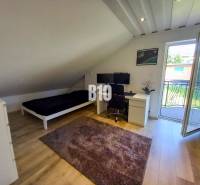 Podkrovní pokoj s pracovním stolem, postelí a balkónovými dveřmi v rodinném domě.