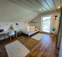 Dětský pokoj v podkroví rodinného domu s postelí, stolem a dekoracemi.