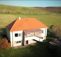 Rodinný dům v Dobré Vodě se šikmou střechou, obklopený zelení a loukami.