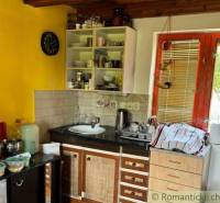 Kuchyně v chatě s dřevěným stropem a žlutou stěnou, vybavená základním nádobím.