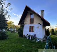 Chata v Sološnici s upravenou zahradou, obklopená stromy a jasnou oblohou.