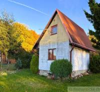 Chata v Sološnici obklopená zelení, se sedlovou střechou a udržovaným trávníkem.
