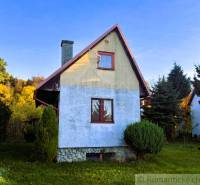 Chata v Sološnici obklopená zelení s modrou omítkou a šikmou střechou.