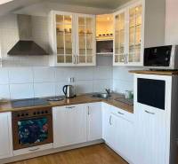 Kuchyně v 3-pokojovém bytě s dřevěnou podlahou, bílými skříňkami a úložným prostorem.