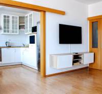 Obývací pokoj v 3-pokojovém bytě s průchodem do kuchyně a nástěnnou televizí.