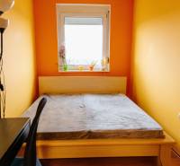 Ložnice s postelí, pracovním stolem a oknem ve dvoupokojovém bytě.