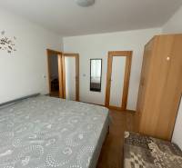 Ložnice s postelí, skříní a zrcadlem v rodinném domě s podlahou s dřevěným dekorem.