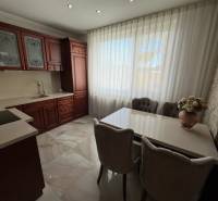 Kuchyně s tmavými skříňkami, bílými závěsy a květinovou dekorací v rodinném domě.