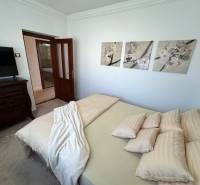 Ložnice rodinného domu s dekorativními obrazy na stěně, čalouněným nábytkem a dveřmi.