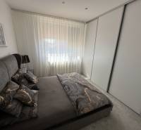 Ložnice v rodinném domě s tmavým ložním prádlem a velkou skříní.