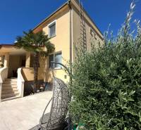 Rodinný dům v Komárně s terasou, zahradním křeslem a palmovým stromem na dvoře.