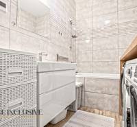 Koupelna ve 3-pokojovém bytě s vanou, dlaždicemi a podlahou s dřevěným dekorem.