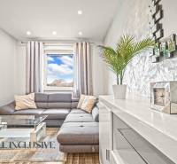 Obývací pokoj s šedou sedačkou, skleněným stolkem a podlahou s dřevěným dekorem.