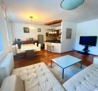 Obývací pokoj s kuchyní v 3pokojovém bytě, vybavení zahrnuje sedačku, stůl a televizi.