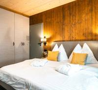 Ložnice v 2-pokojovém bytě s postelí, skříní a stěnou s dřevěným dekorem.