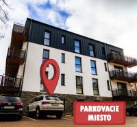 Bytový dům na Lúčnej ulici ve Štrbě s vyznačeným parkovacím místem v popředí.