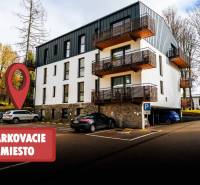 Moderní bytový dům na Lúčnej ulici v Štrbě s parkovacím prostorem před budovou.