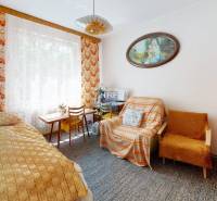 Pokoj v rodinném domě s postelí, kobercem, křeslem a obrazem na stěně.