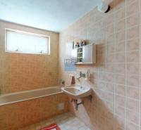 Koupelna v rodinném domě se starším obkladem, vanou a umyvadlem.