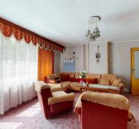 Obývací pokoj v rodinném domě s květinovou tapetou, měkkou sedací soupravou a dlouhým závěsem.